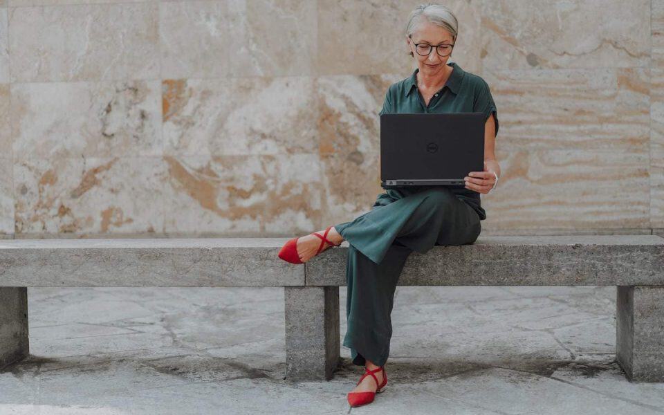 Barbara Schemel arbeitet auf einer Steinbank an ihrem Laptop